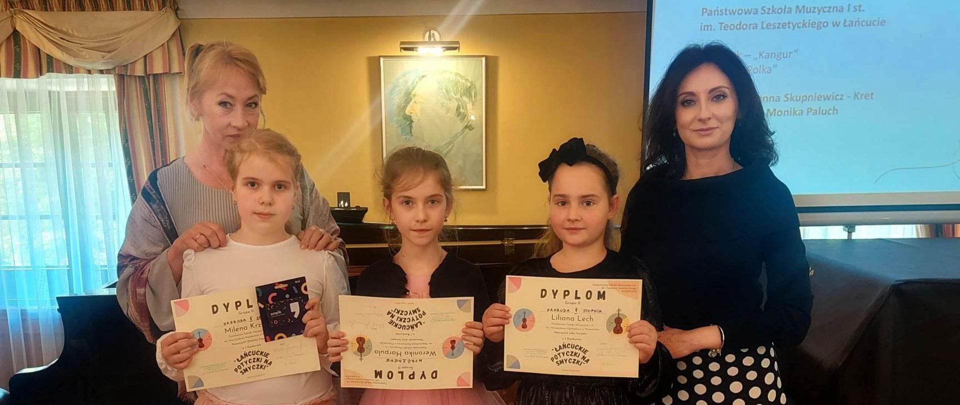 Sala koncertowa PSM I st. w Łańcucie. Na zdjęciu p. Elżbieta Trojak oraz p. Julia Surmacz i 3 uczennice trzymające dyplomy otrzymane na konkursie.