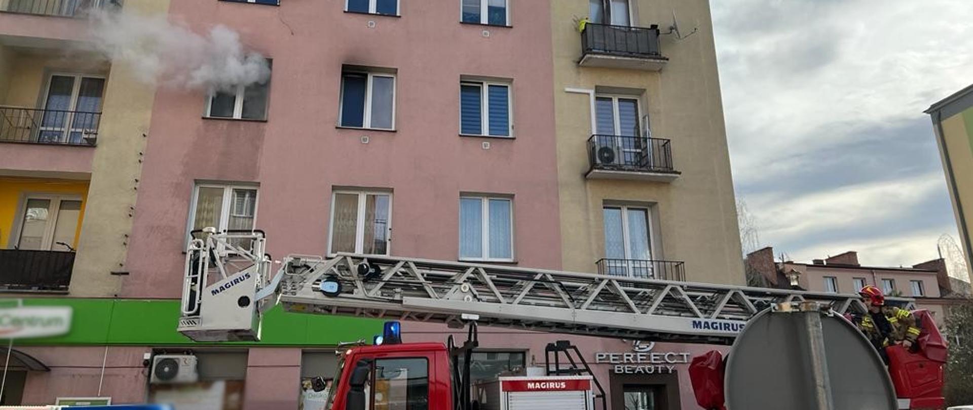 Dym wydobywa się z mieszkania a przed blokiem samochody pożarnicze.