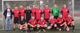Zdjęcie grupowe drużyny KP PSP Białogard. W tle bramka. Strażacy w strojach sportowych czerwono czarnych.
