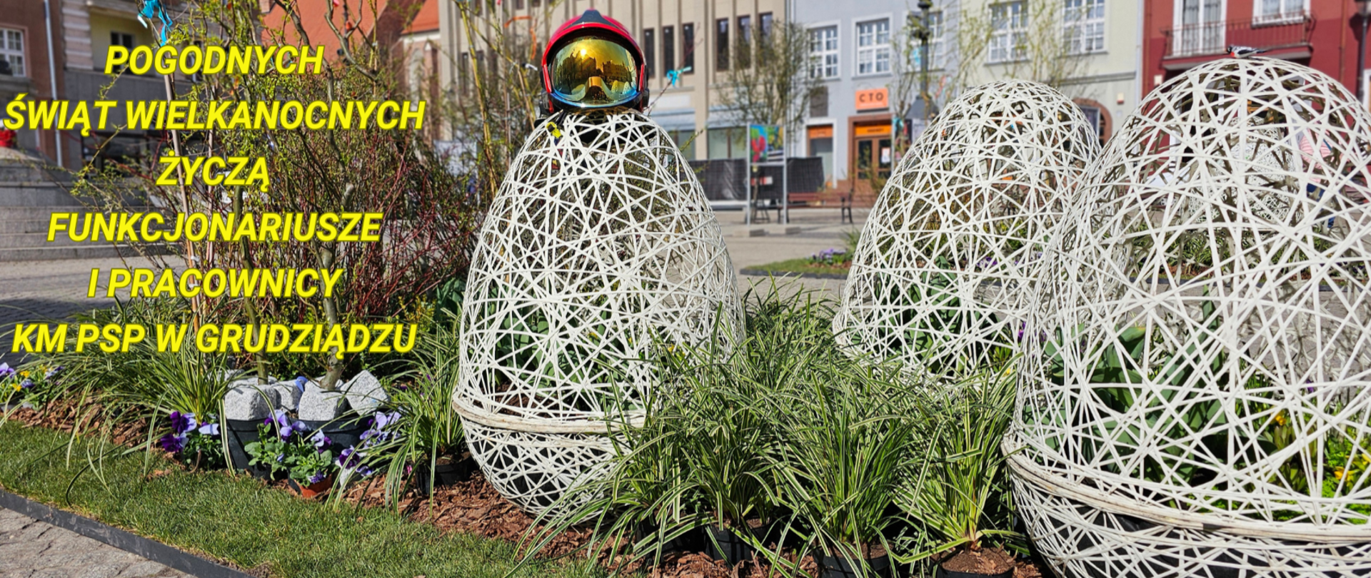 Wielkanocna plenerowa instalacja składająca się z trzech konstrukcji w postaci jaj oraz roślin zielonych z tekstem życzeń