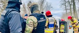 Zdjęcie przedstawia wszystkie służby biorące udział w ćwiczeniach, w tyle samochód po wypadku leżący na boku, w tle las 