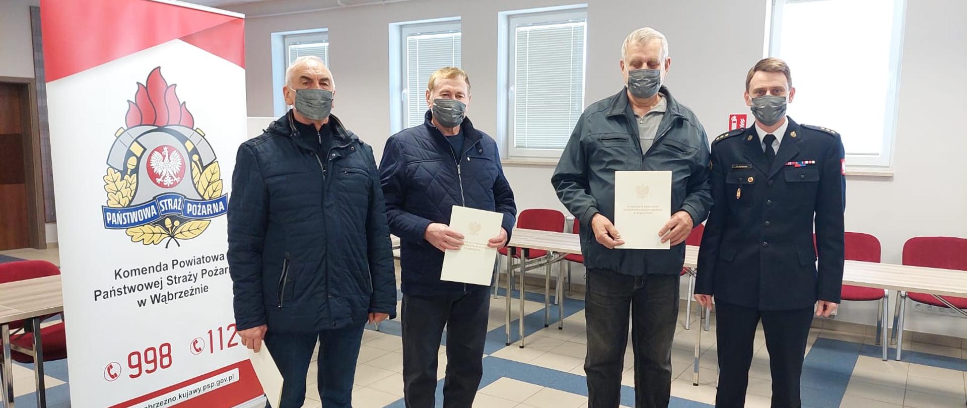 Wręczenie decyzji o przyznaniu świadczenia ratowniczego. Na zdjeciu trzech druchow OSP z decyzjami o przyananiu swiadczenia oraz p.o. Komendatnt Powiatowy PSP w Wabrzeznie.