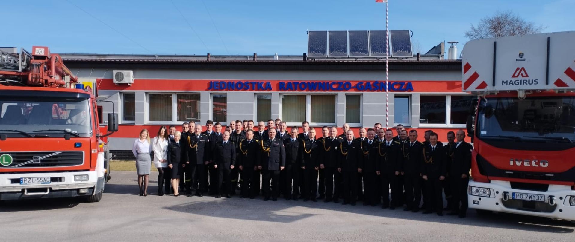 Na zdjęciu funkcjonariusze KP PSP oraz JRG na tle JRG po bokach ustawione są samochody strażackie.