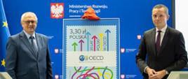 Plakat ze znaczkiem w centralnej części zdjęcia, po lewej stronie znajduje się Minister, po prawej Prezes
