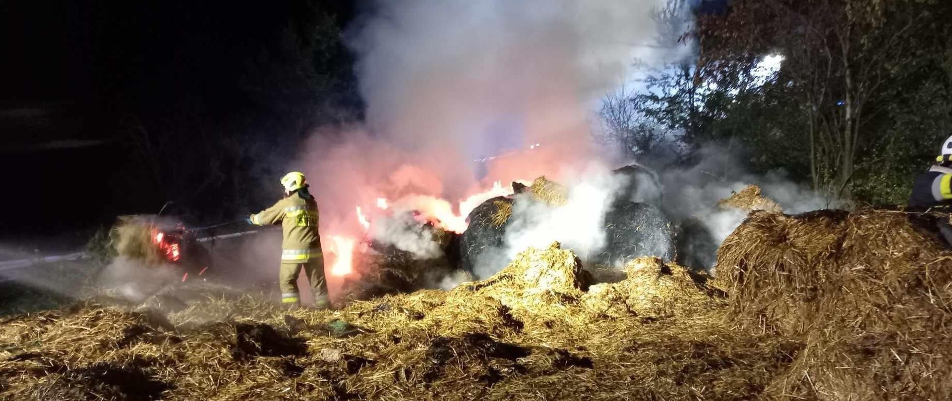 Na zdjęciu widać strażaka przerzucającego słomę podczas pożaru.