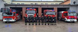 Strażacy z JRG3 w szeregu w czarnych ubraniach koszarowych, w tle samochody pożarnicze i budynek JRG