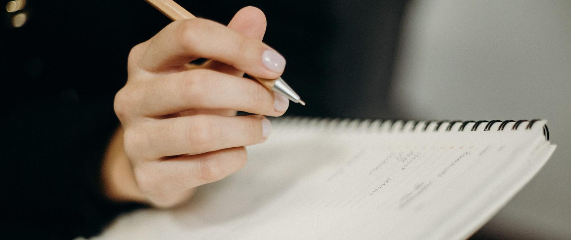 Ręka osoby trzymającej długopis, zapisującej notatki.
