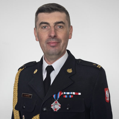 Komendant PSP na zdjęciu w mundurze wyjściowym. Zdjęcie obejmuje popiersie Komendanta. Na mundurze widoczne odznaczenia pożarnicze oraz imiennik
