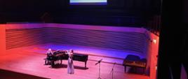 Uczennica gra na oboju stojąc przed fortepianem, akompaniatorka gra na fortepianie na scenie sali koncertowej PSM