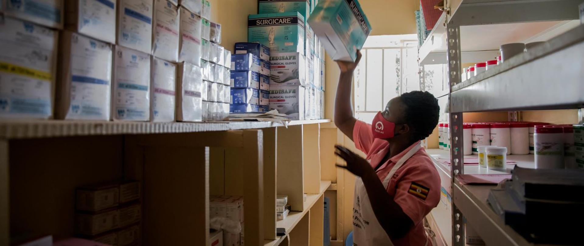 kobieta w maseczce z logo zdejmuje z półki pudełka 