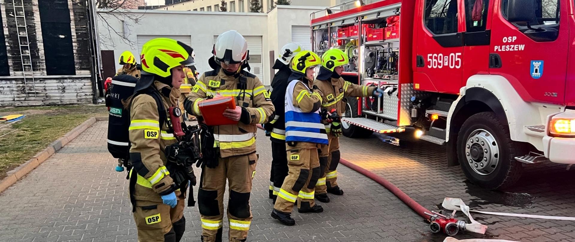 Strażacy czekający przed wejściem do budynku podczas ćwiczeń z pożarów wewnętrznych