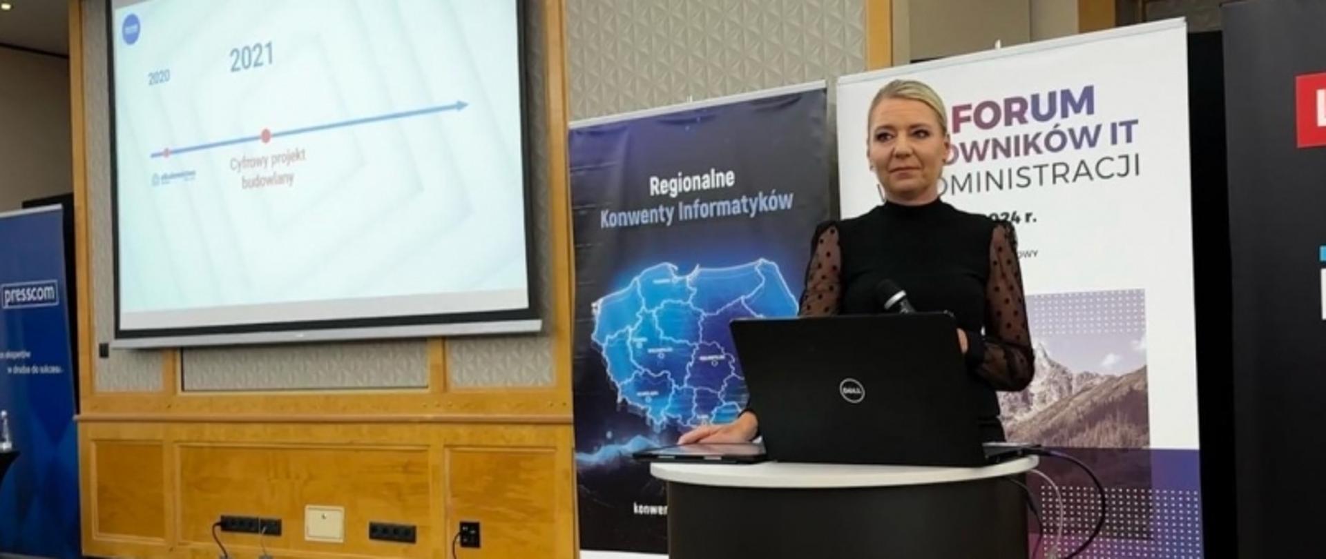 Dorota Cabańska z Głównego Urzędu Nadzoru Budowlanego podczas prezentacji na konferencji IT dla administracji publicznej. Wystąpienie dotyczy cyfryzacji i nowoczesnych rozwiązań technologicznych. W tle widoczne są slajdy prezentacji oraz banery partnerów wydarzenia, takich jak Lenovo, Intel i inni. Publiczność słucha prelekcji w sali konferencyjnej.