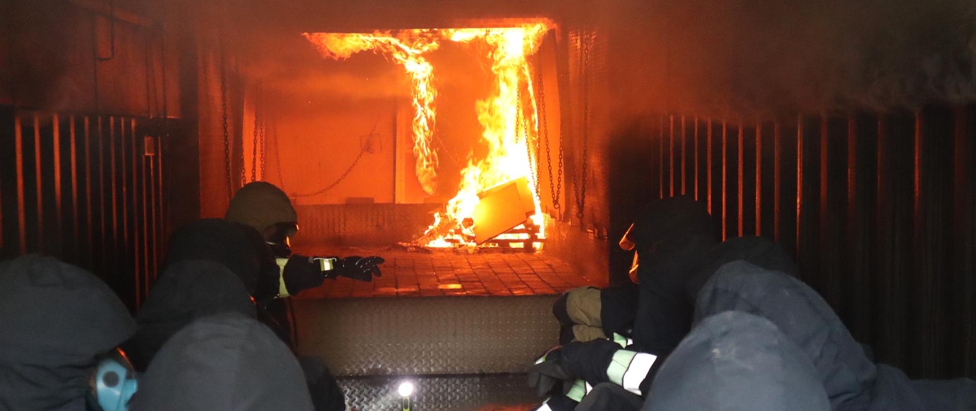 Zdjęcie przedstawia strażaków PSP z terenu województwa pomorskiego, siedzących wewnątrz kontenera i obserwujących rozwój pożaru.