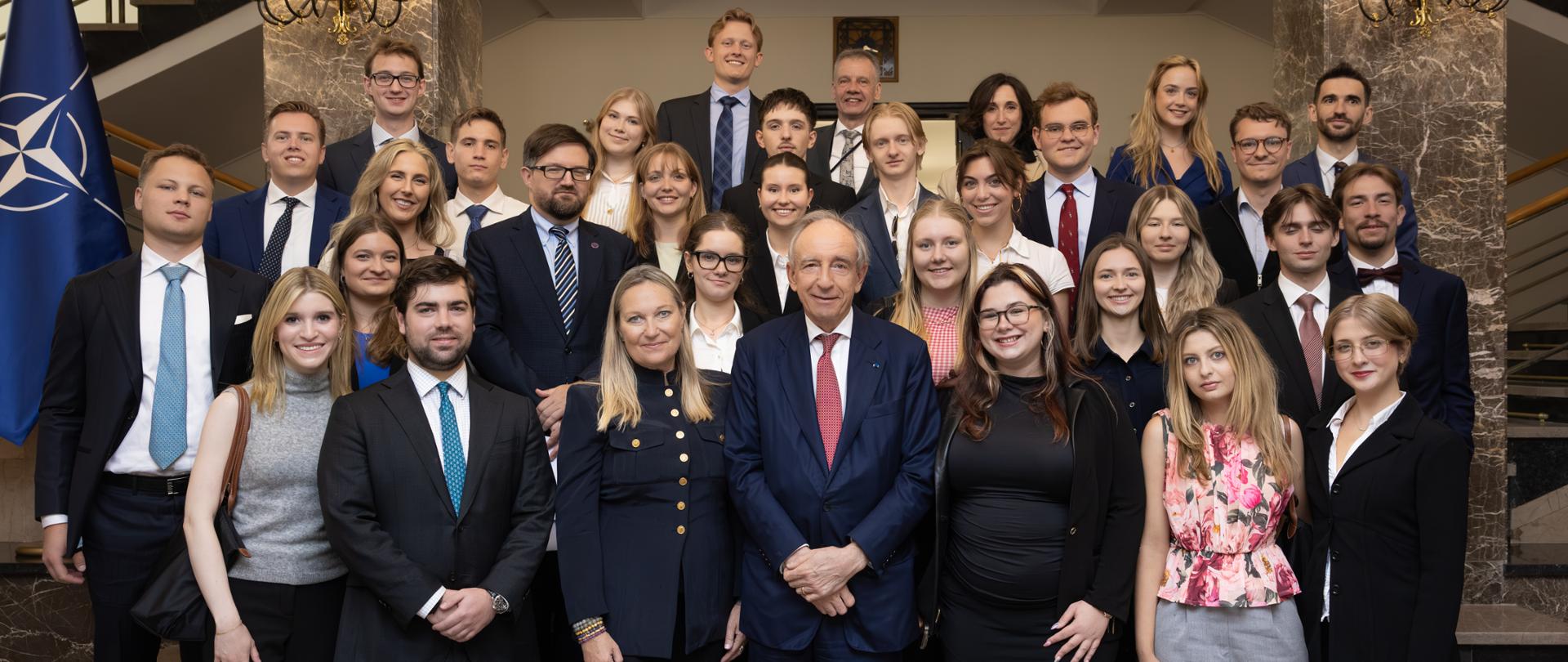 Na zdjęciu stoi duża grupa uczestników spotkania z wiceministrem Władysławem Teofilem Bartoszewskim. Zdjęcie zostało zrobione na schodach. 