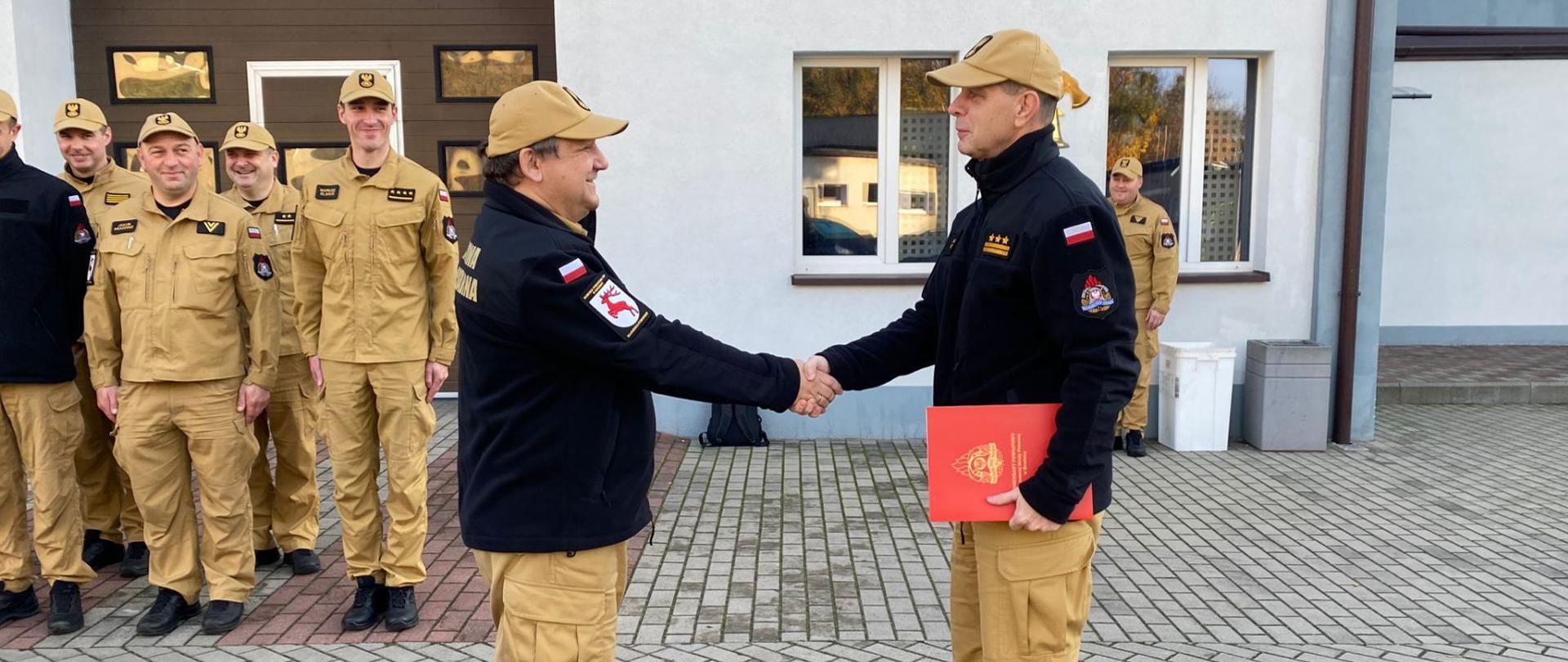 Zdjęcie przedstawia st. bryg. Andrzeja Góreckiego Komendanta Powiatowego PSP w Brodnicy wręczającego st. asp. Jackowi Szałkowskiemu list gratulacyjny wraz z informacją o przyznaniu nagrody z okazji jubileuszu pracy zawodowej.