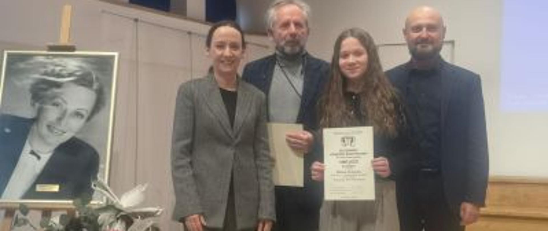 
Zdjęcie  kolorowe: od lewej stoją: dr hab. Agata Szymczewska prof. UMFC, ubrana szary garnitur, obok mgr Tomasz Szymczewski (fortepian-akompaniator )ubrany w czarny garnitur i szary golf, obok uczennica  Milena Kukulska, ubrana w czarną bluzkę i stalowe spodnie, obok  mgr Artur Pastuszyński (nauczyciel  Mileny Kukulskiej) ubrany w czarny garnitur. 