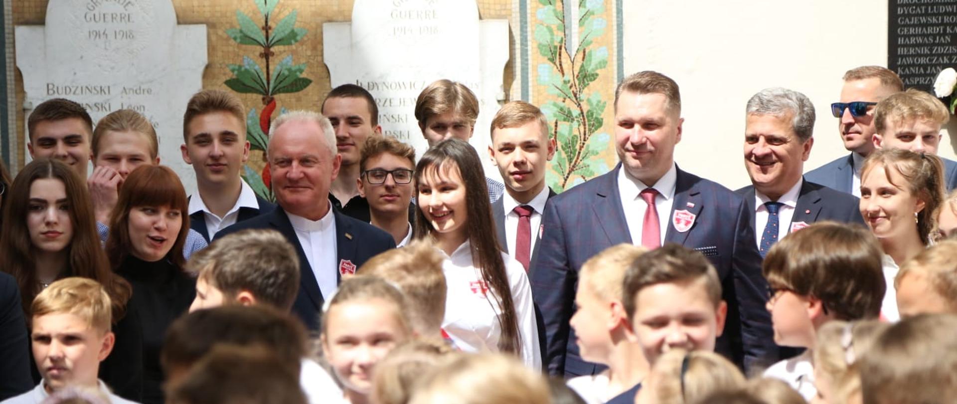 Minister Przemysław Czarnek, a wokół grupa odświętnie ubranych uczniów. Po lewej stronie rektor KUL, a po prawej ambasador RP we Francji. 