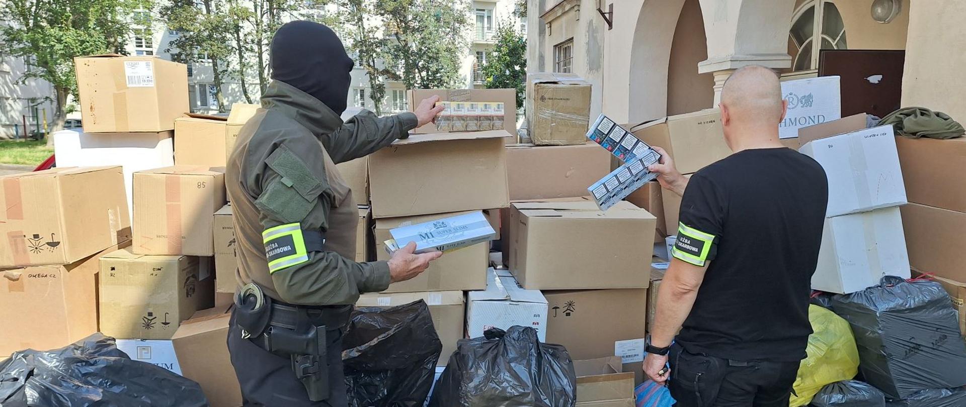 Funkcjonariusze Służby Celno-Skarbowej przy kartonach z papierosami.