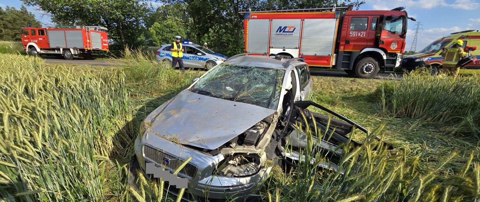 Samochód na polu, za nim samochody strażackie