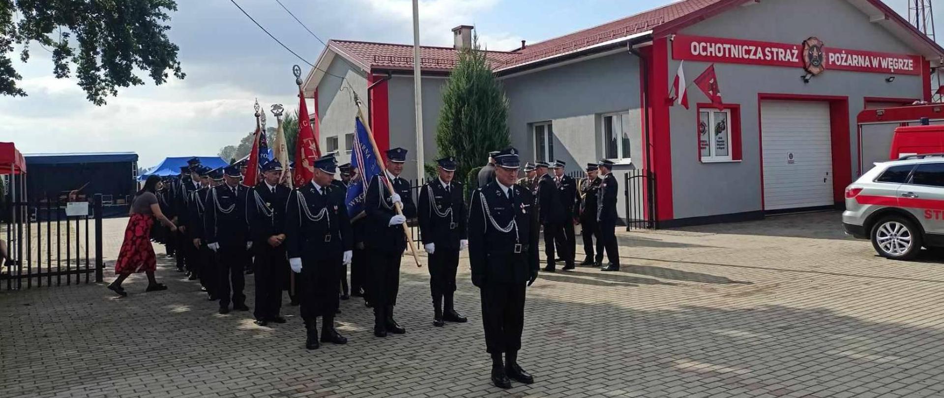 zgrupowanie pocztów sztandarowych na tle remizy OSP w Węgrze