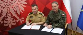 Pan Komendant i Dowódca podpisują porozumienie, przy stole, w sali Komendy Wojewódzkiej PSP w Poznaniu. W tle ścianka KW, roll upp WOT. 