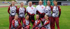 Pamiątkowe zdjęcie zawodniczek pożarniczej drużyny PSP (8 kobiet) w towarzystwie trenera oraz kierownika drużyny stojących na murawie stadionu