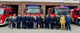 Emeryt Zenon, Funkcjonariusze z KP PSP, oraz zaproszeni goście na wspólnym zdjęciu przed budynkiem Jednostki Ratowniczo Gaśniczej w Pucku. Na drugim planie samochody gaśnicze z JRG
