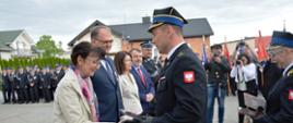 Na pierwszym planie Komendant Powiatowy Państwowej Straży Pożarnej w Radomsku wręcza pamiątkową statuetkę Pani Wiesławie Janosik. 