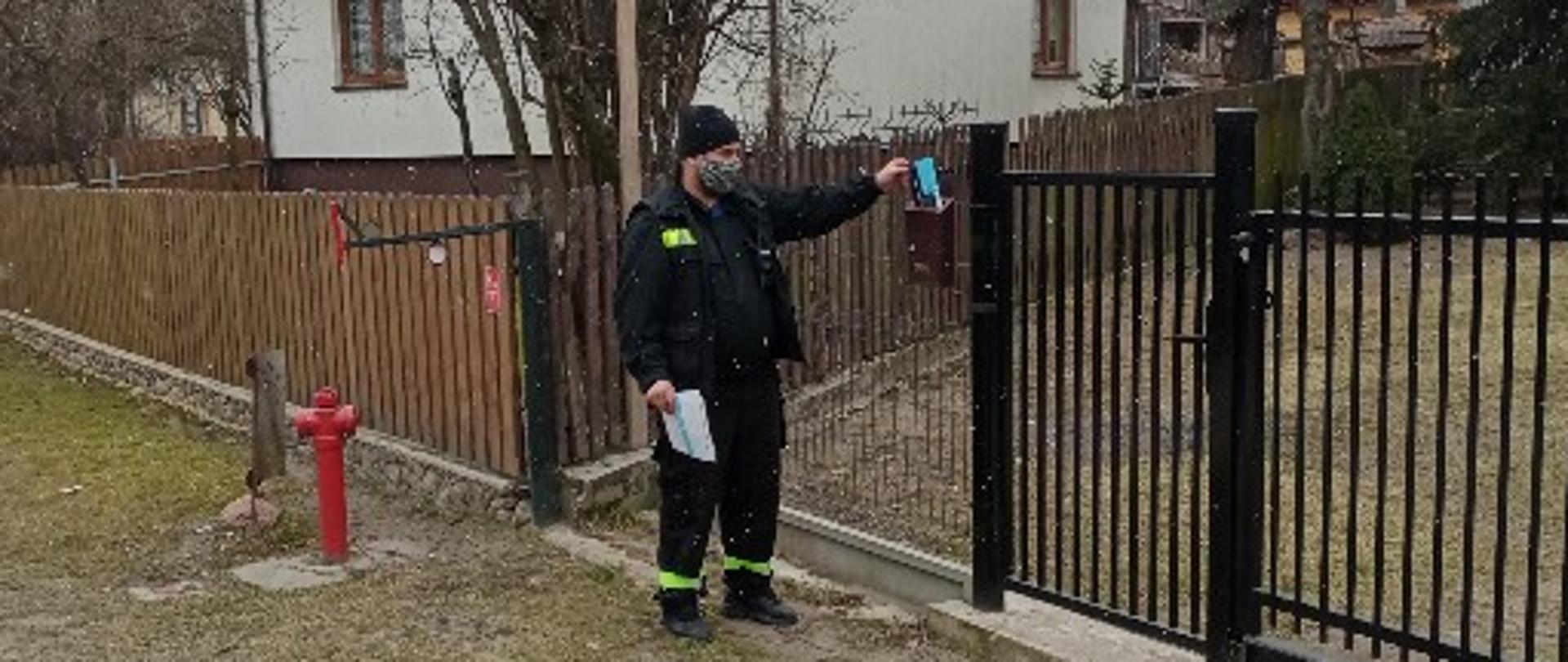 Akcja informacyjna na temat szczepień przeciwko COVID-19 strażak wrzuca ulotkę do skrzynki pocztowej