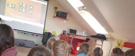 Dzieci siedząc oglądaja w sali ognik filmiki edukacyjne z zakresu ochrony przeciwpożarowej