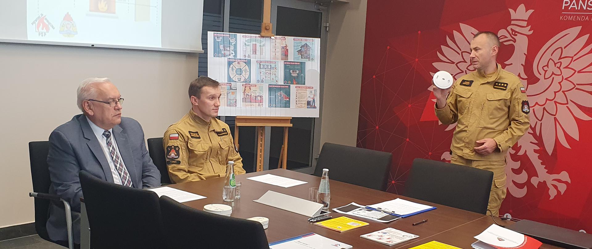 Funkcionariusz przedstawiajacy zasade dzialania czujki tlenku wegla.