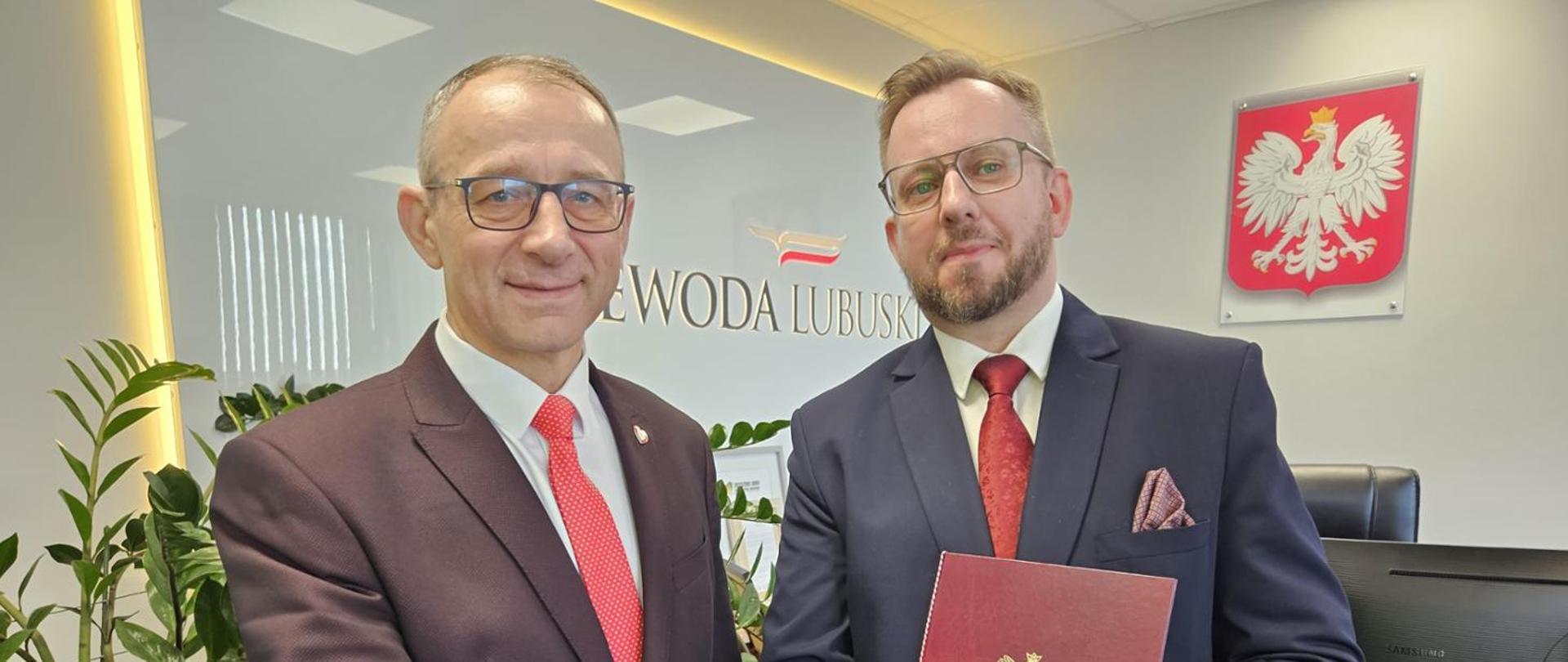 Dwaj mężczyźni w garniturach stoją obok siebie. W tle widać napis Wojewoda Lubuski z godło państwowe.