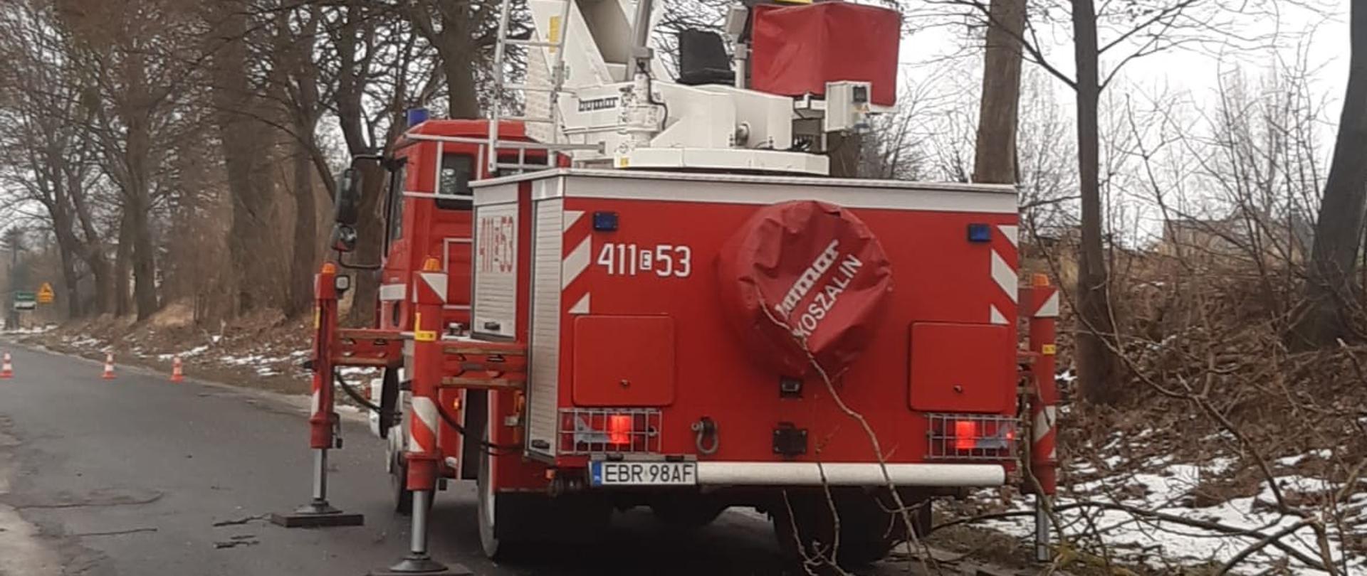 Samochód SHD-25 na pasie jezdni z rozwiniętą drabiną, droga zablokowana przez konary drzew.