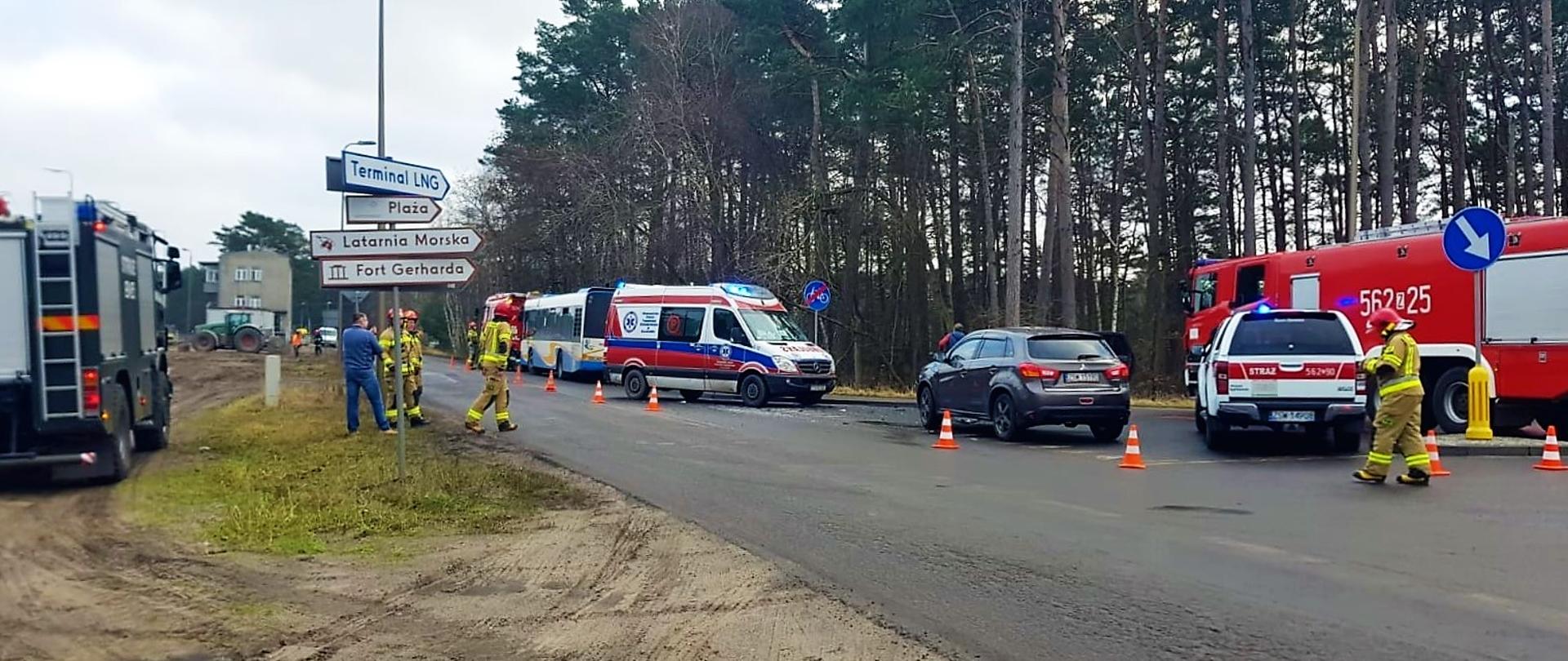 Uszkodzony autobus oraz samochód osobowy stoją ja ulicy Barlickiego. Obok nich stoją 3 samochody gaśnicze, 1 samochód rozpoznawczo-ratowniczy oraz karetka. Teren zabezpieczają strażacy w mundurach bojowych.