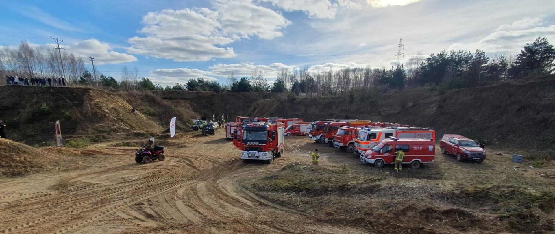 Pojazdy pożarnicze ustawione jeden obok drugiego w półokręgu na terenie kopalni (w dole). Oczekiwanie na rozpoczęcie szkolenia