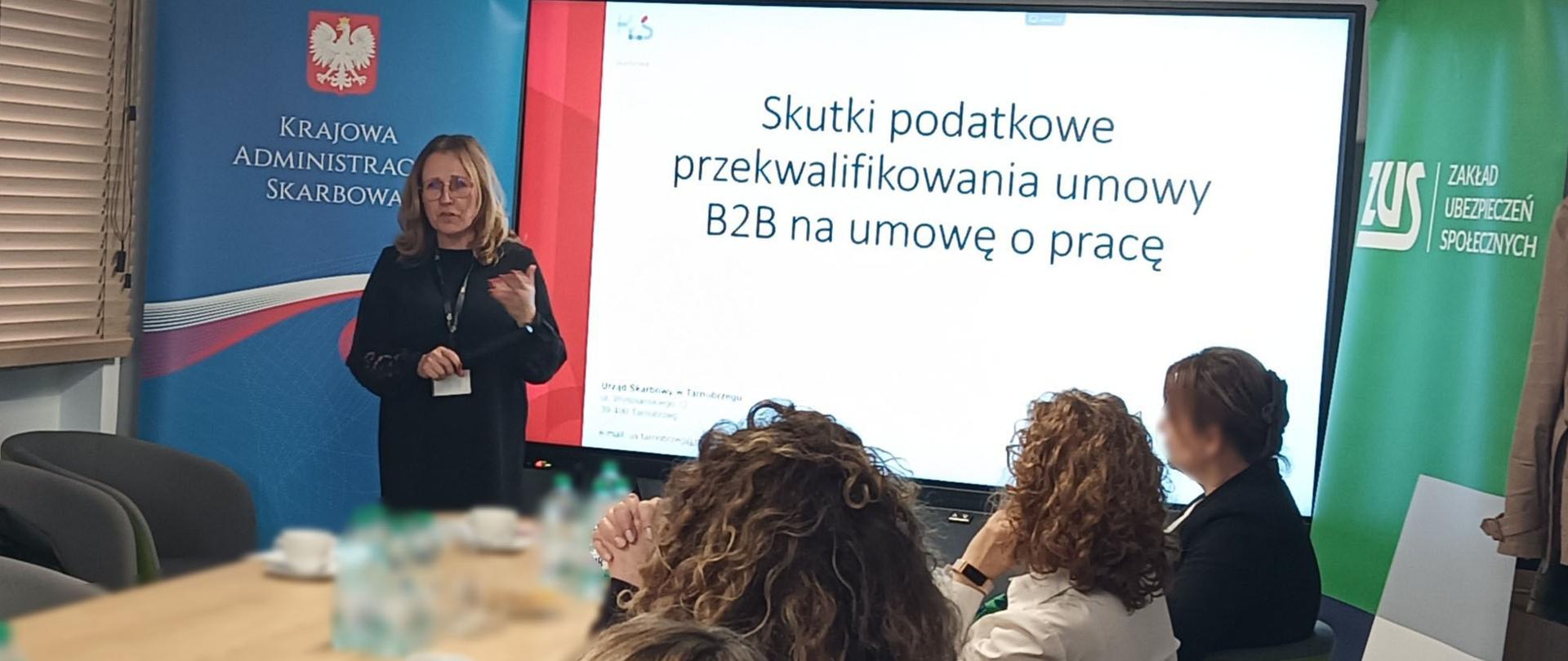 Ekspertka stoi przed uczestnikami spotkania. Na ekranie wyświetlana jest prezentacja.