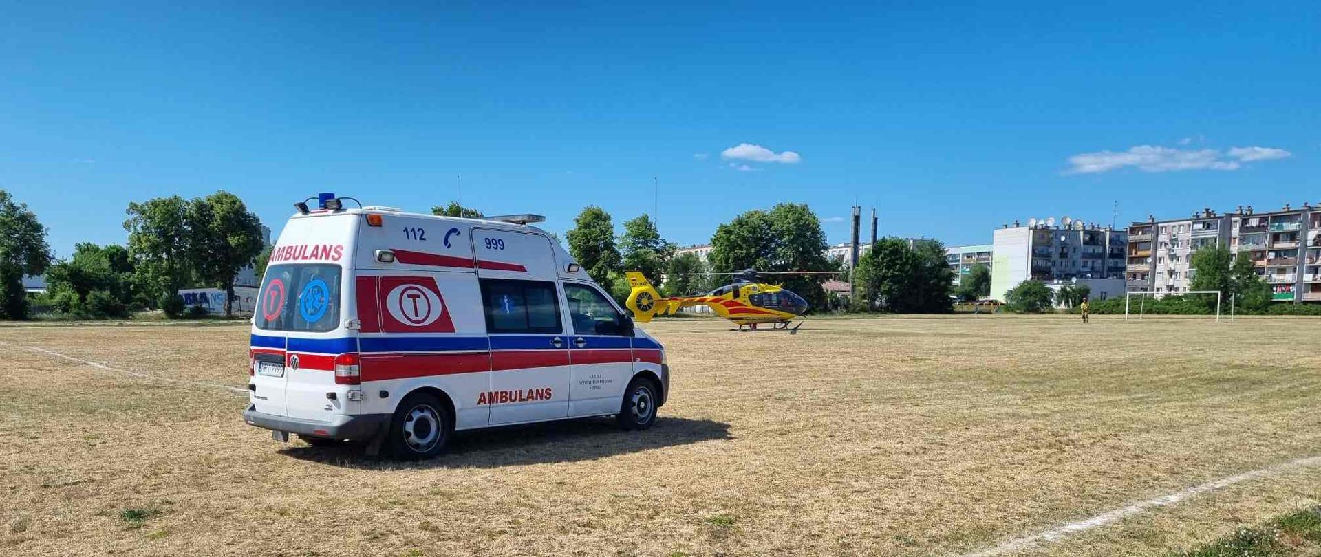 Boisko, stojąca karetka oraz śmigłowiec Lotniczego Pogotowia Ratunkowego.