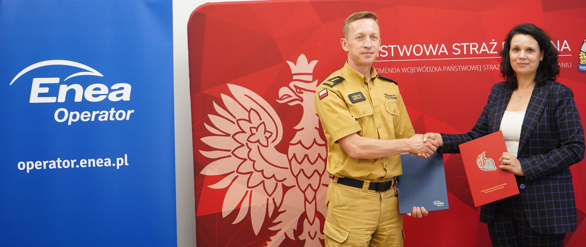 strażak i kobieta w kraciastek marynarce podają sobie dlonie