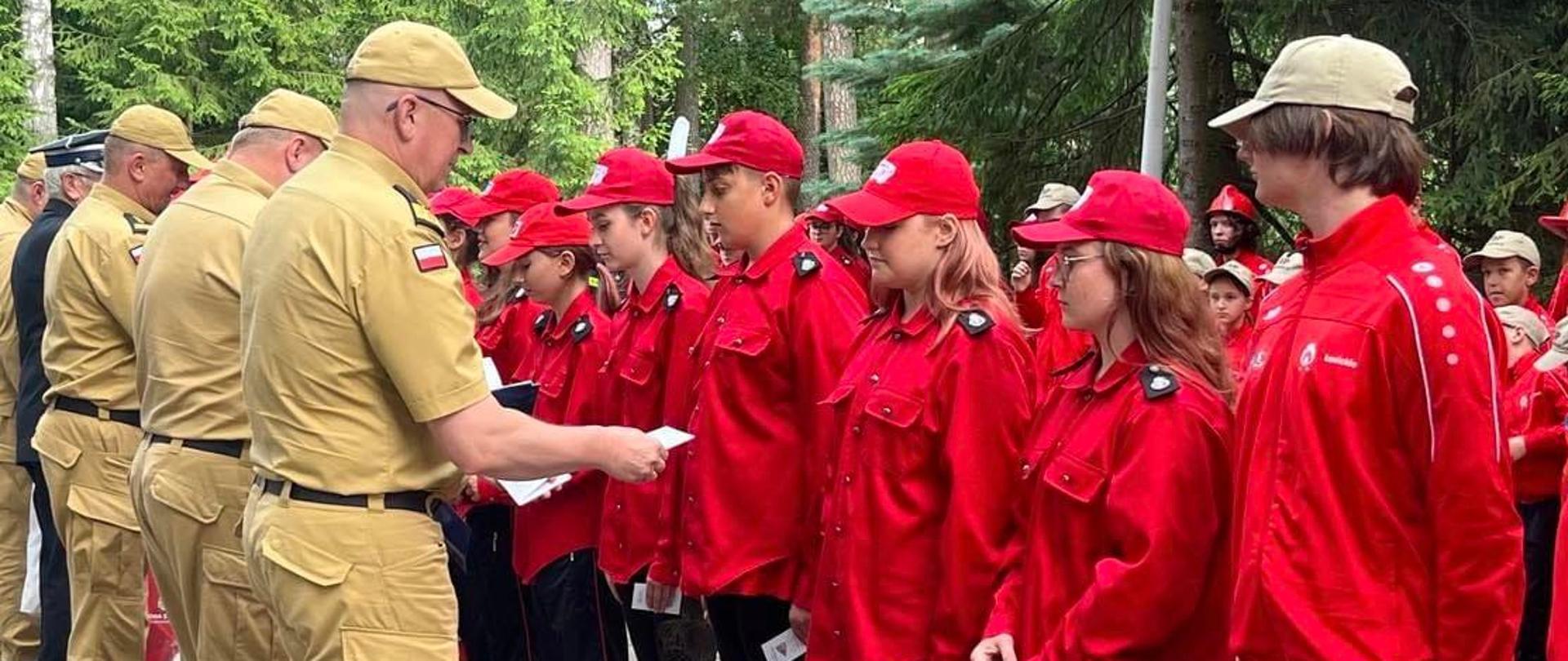 zastępca komendanta głównego PSP, komendant wojewódzki wraz z zastępcą oraz druh OSP wręczają dzieciom z MDP odznaki 