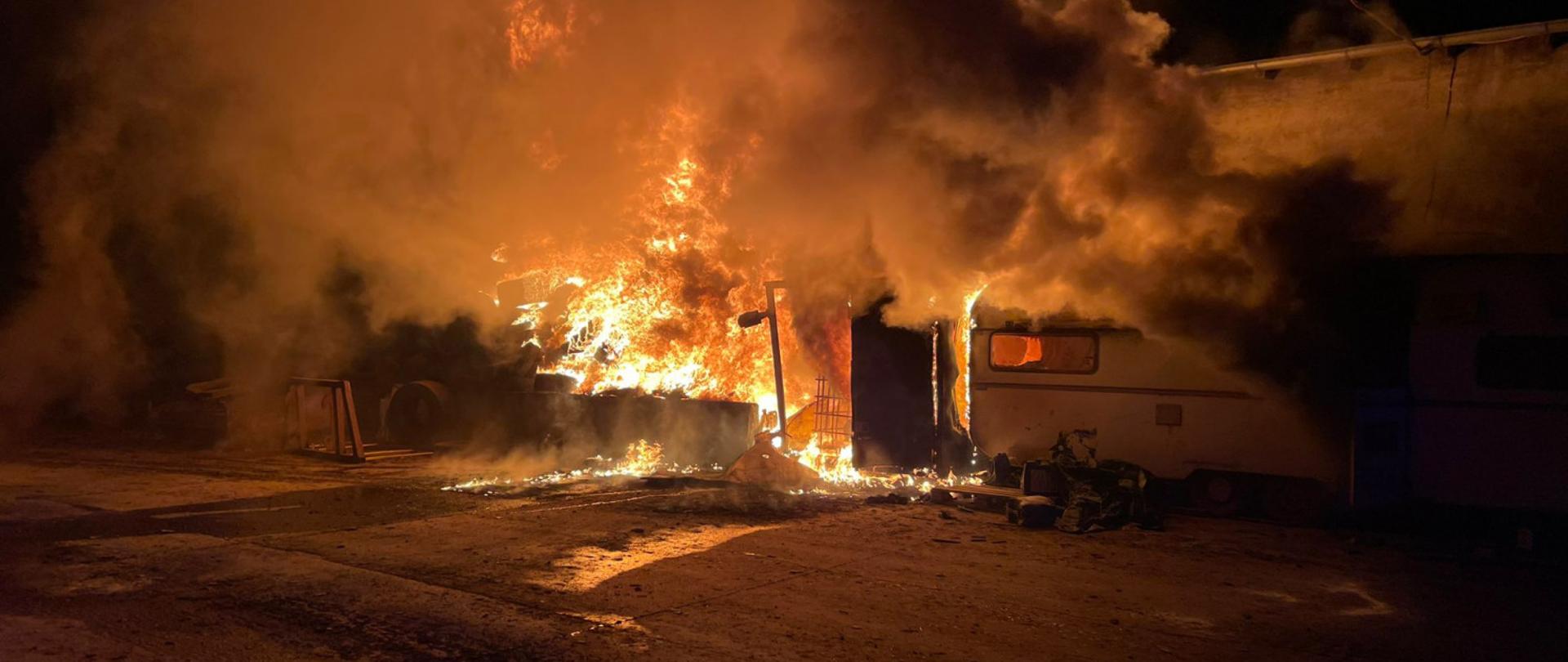 Płomienie ognia obejmują zbiornik z paliwem, opony oraz przyczepę kempingową. Panuje duże zadymienie.