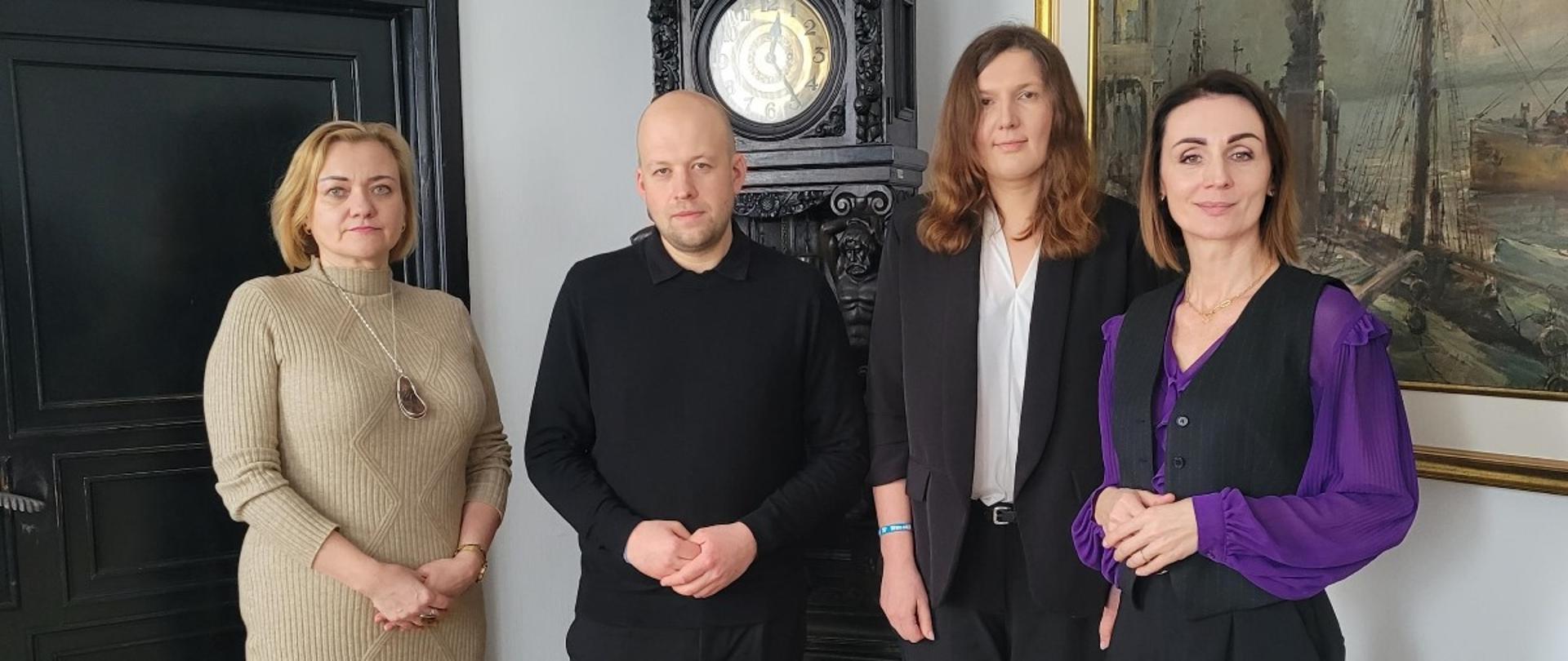 cztery osoby, w tym trzy kobiety stoją w pokoju (gabinecie wojewody) na tle starego zegara