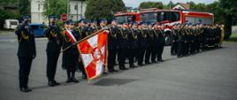 Pododdział strażaków na tle pojazdów pożarniczych