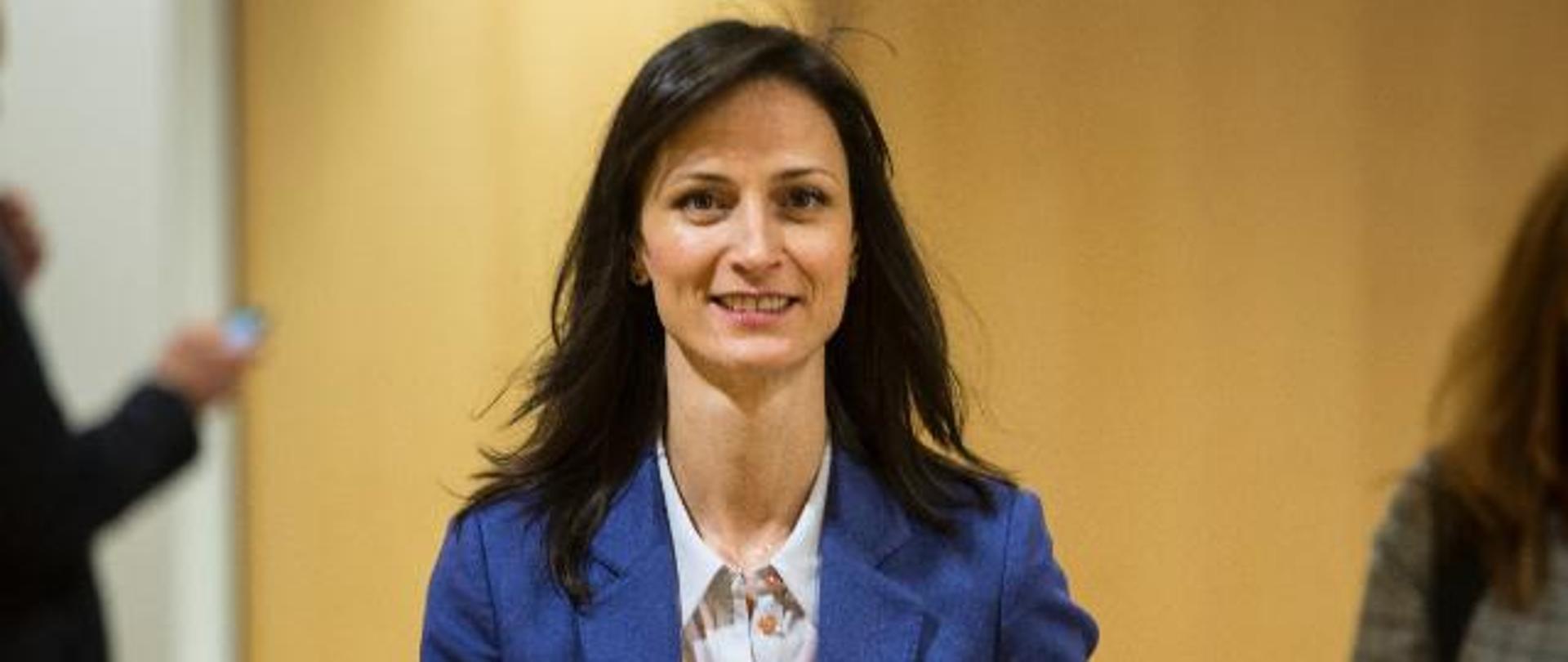 A woman in a blue jacket carrying documents

