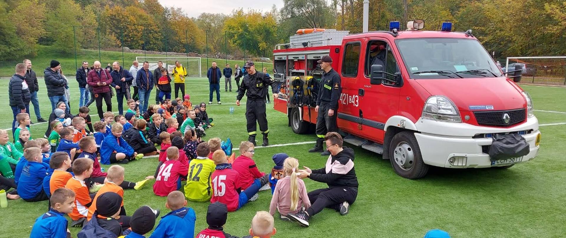 Na zdjęciu znajdują się dzieci oraz strażacy z KP PSP w Chełmnie podczas prelekcji dotyczącej zasad bezpieczeństwa w lesie. Zdjęcie wykonano na boisku "Sahara" w Chełmnie.