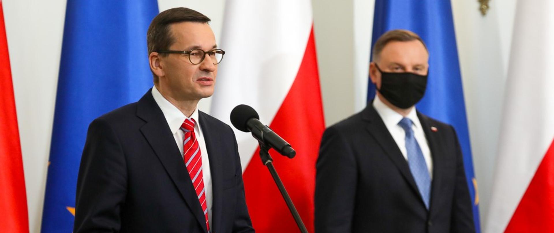 Premier Mateusz Morawiecki przemawia, obok stoi prezydent Andrzej Duda.