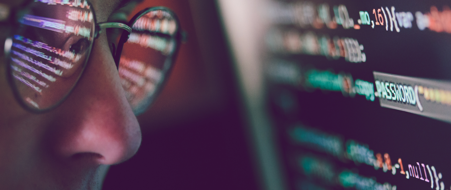 Zbliżenie na twarz mężczyzny w okularach (w domyśle ekspert cyberbezpieczeństwa) przyglądającego się ekranowi, na którym wyświetla się ciąg znaków, w tym słowo password (hasło).