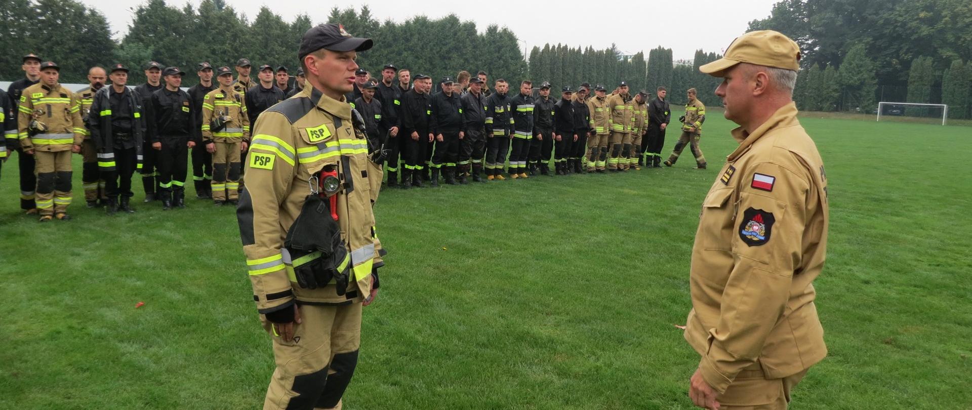 Zdjęcie przedstawia st. kpt. Roberta Czarneckiego Zastępcę Dowódcy JRG w Brodnicy składającego meldunek o zakończeniu ćwiczeń st. bryg. Robertowi Wiśniewskiemu Zastępcy Kujawsko-Pomorskiego Komendanta Wojewódzkiego PSP. W oddali strażacy uczestniczący w ćwiczeniach.