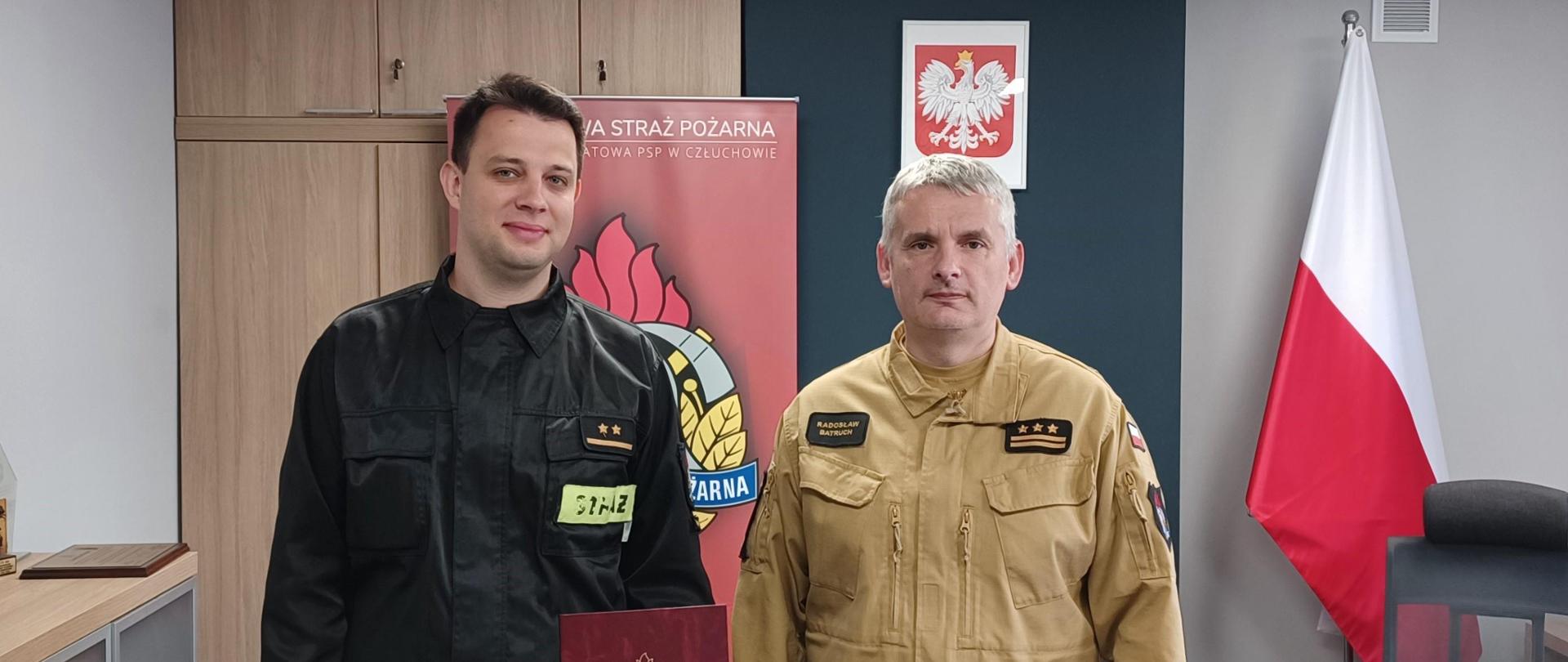 Komendant Powiatowy Państwowej Straży Pożarnej w Człuchowie st. bryg. Radosław Batruch stoi w gabinecie i wręcza akt mianowania na stanowisko zastępcy dowódcy Jednostki Ratowniczo - Gaśniczej w Człuchowie mł. kpt. Dawidowi Machnio. 