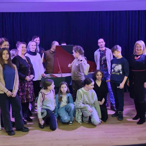 Zdjęcie zbiorowe młodzieży z nauczycielami na scenie po koncercie muzyki dawnej. wszyscy są uśmiechnięci. W tle stoi klawesyn z otwartą klapą. 