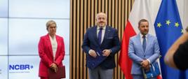 Na zdjęciu na tle flagi Polski i UE stoi Minister Maria Mrówczyńska z Dyrektorem NCBR i Dyrektorem OPI PIB
